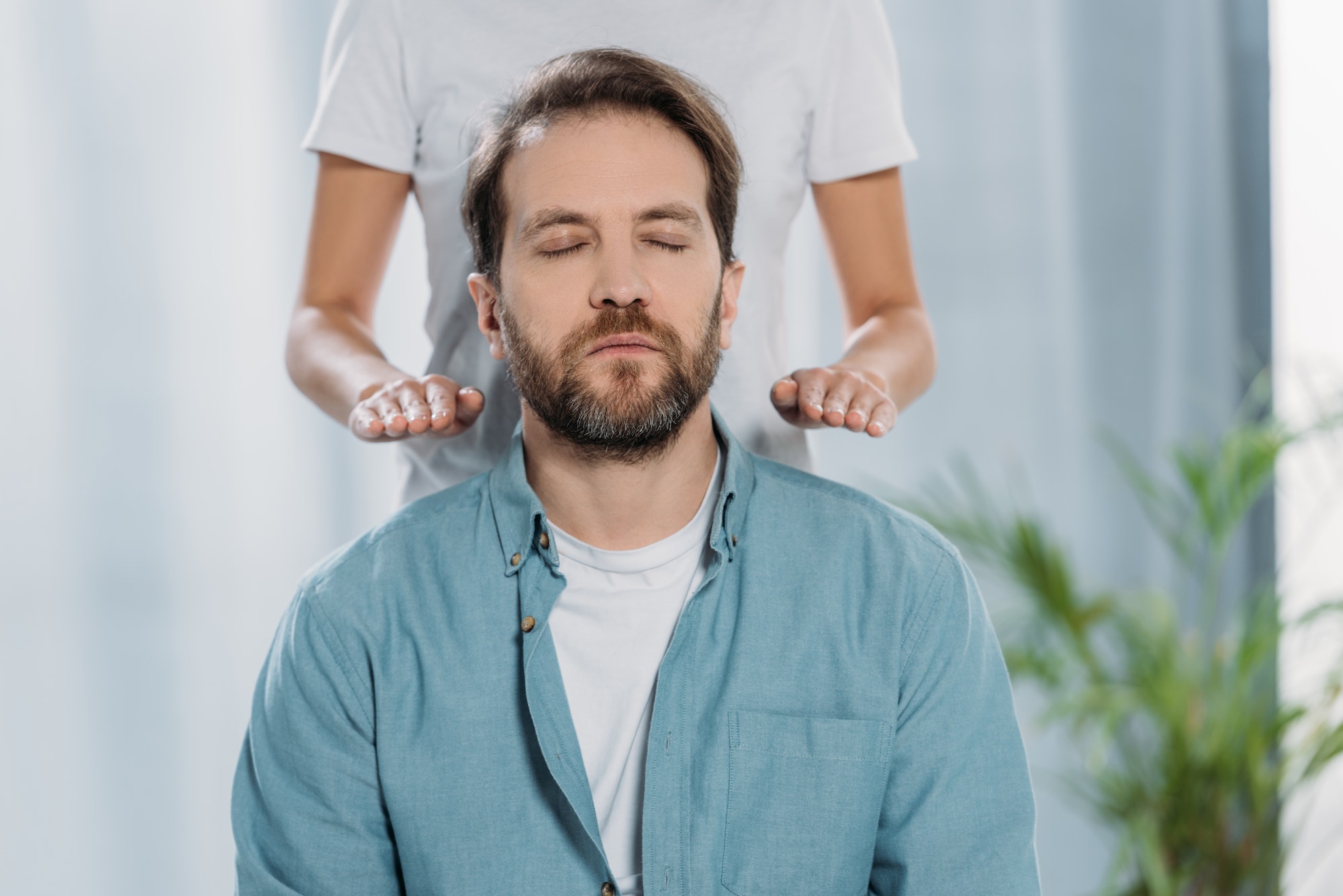 cropped shot of bearded man with closed eyes sitting and receiving reiki healing therapy